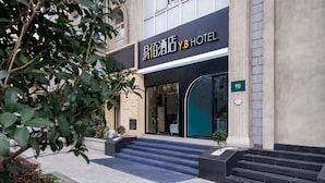 Een hotelentree met een moderne gevel, een trap die naar de ingang leidt, en een bord met de naam van het hotel.