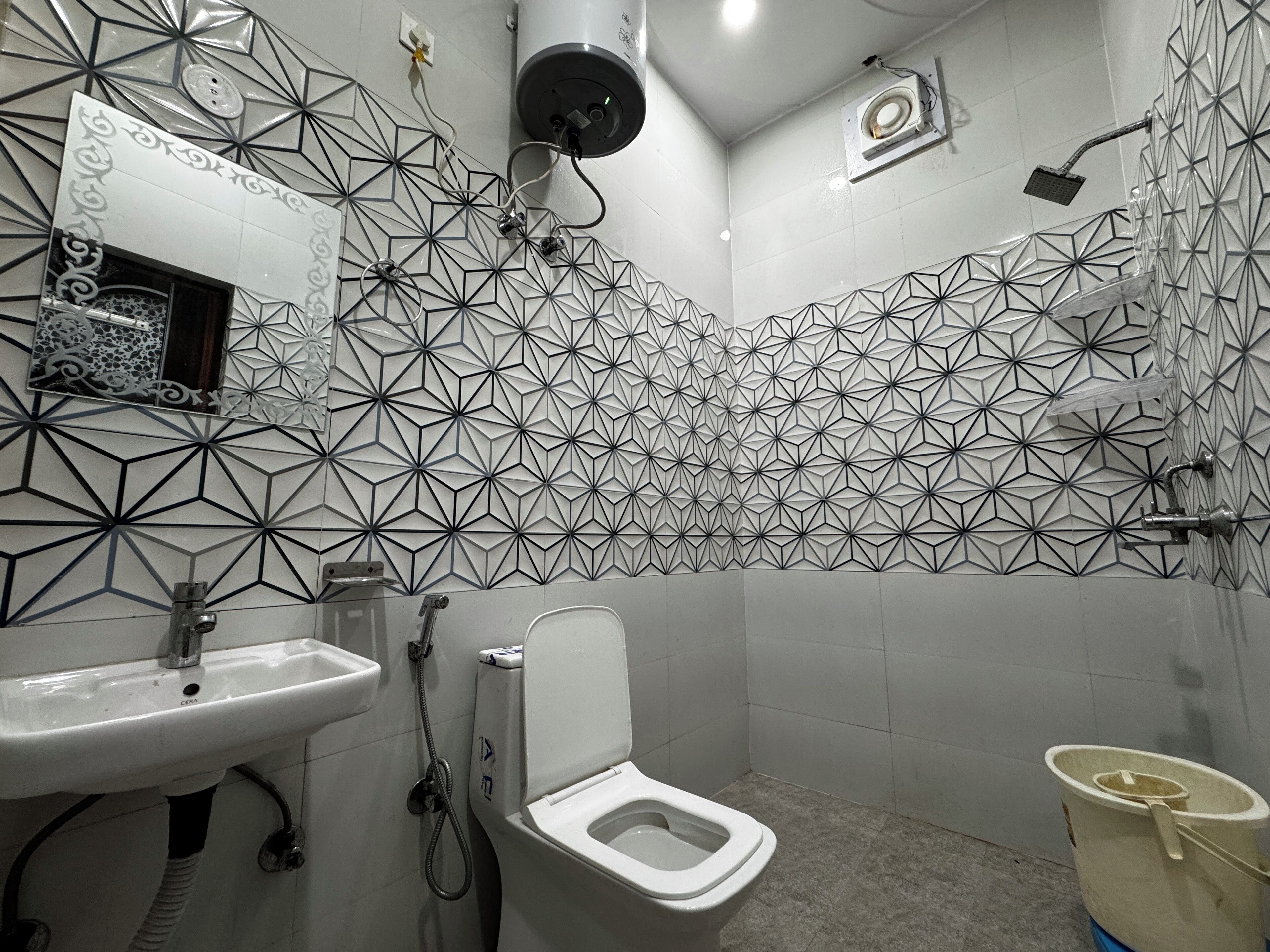 Un baño con un diseño geométrico de azulejos, un lavabo blanco, un inodoro y una ducha.