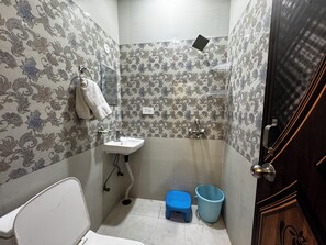 A bathroom with patterned wallpaper, a white sink, a small blue stool, and a blue bucket. - Vrindavani Kunj (Vrindavan)