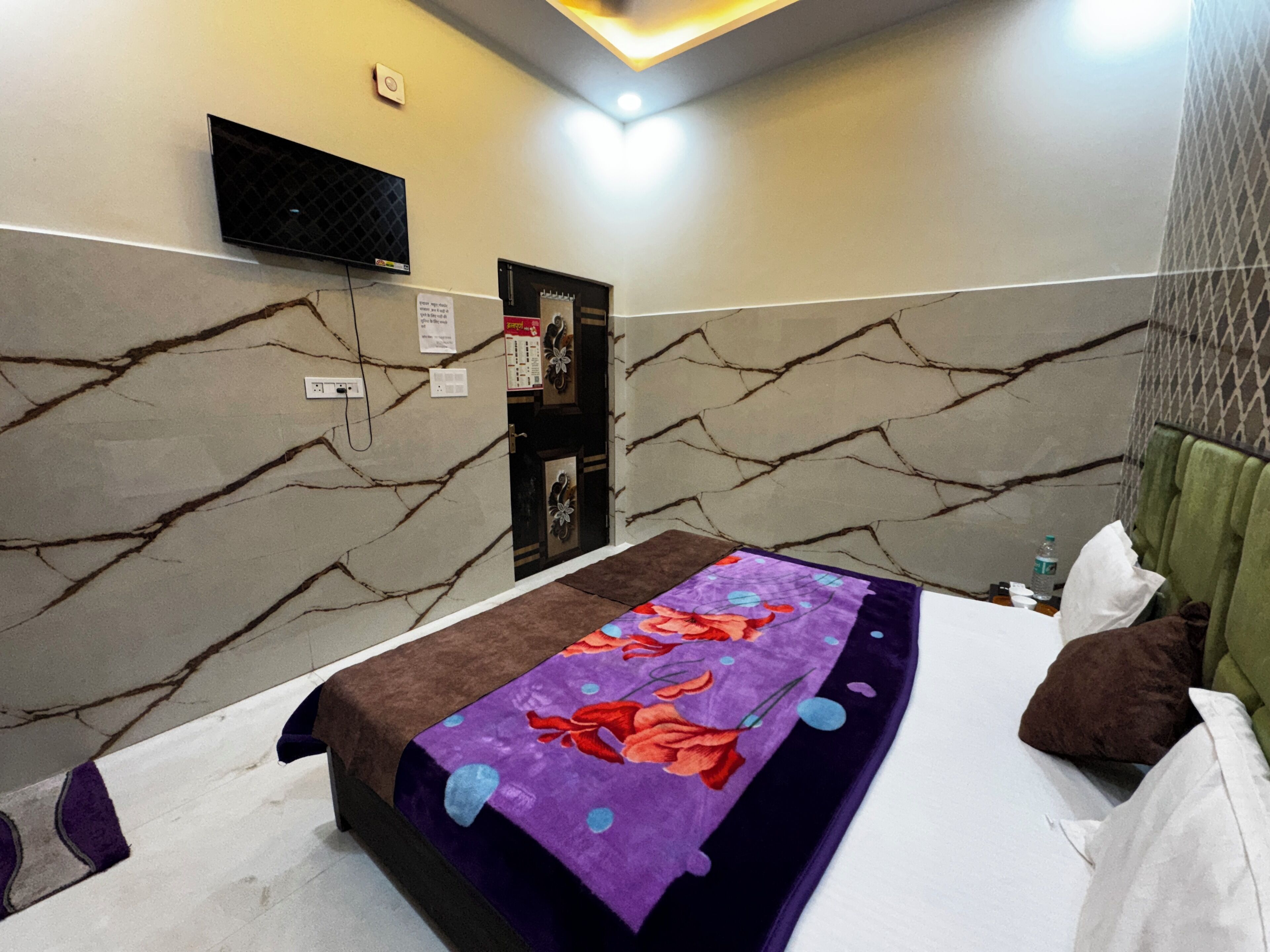 A hotel room with a bed, a flat-screen TV mounted on the wall, and a door with a decorative handle.