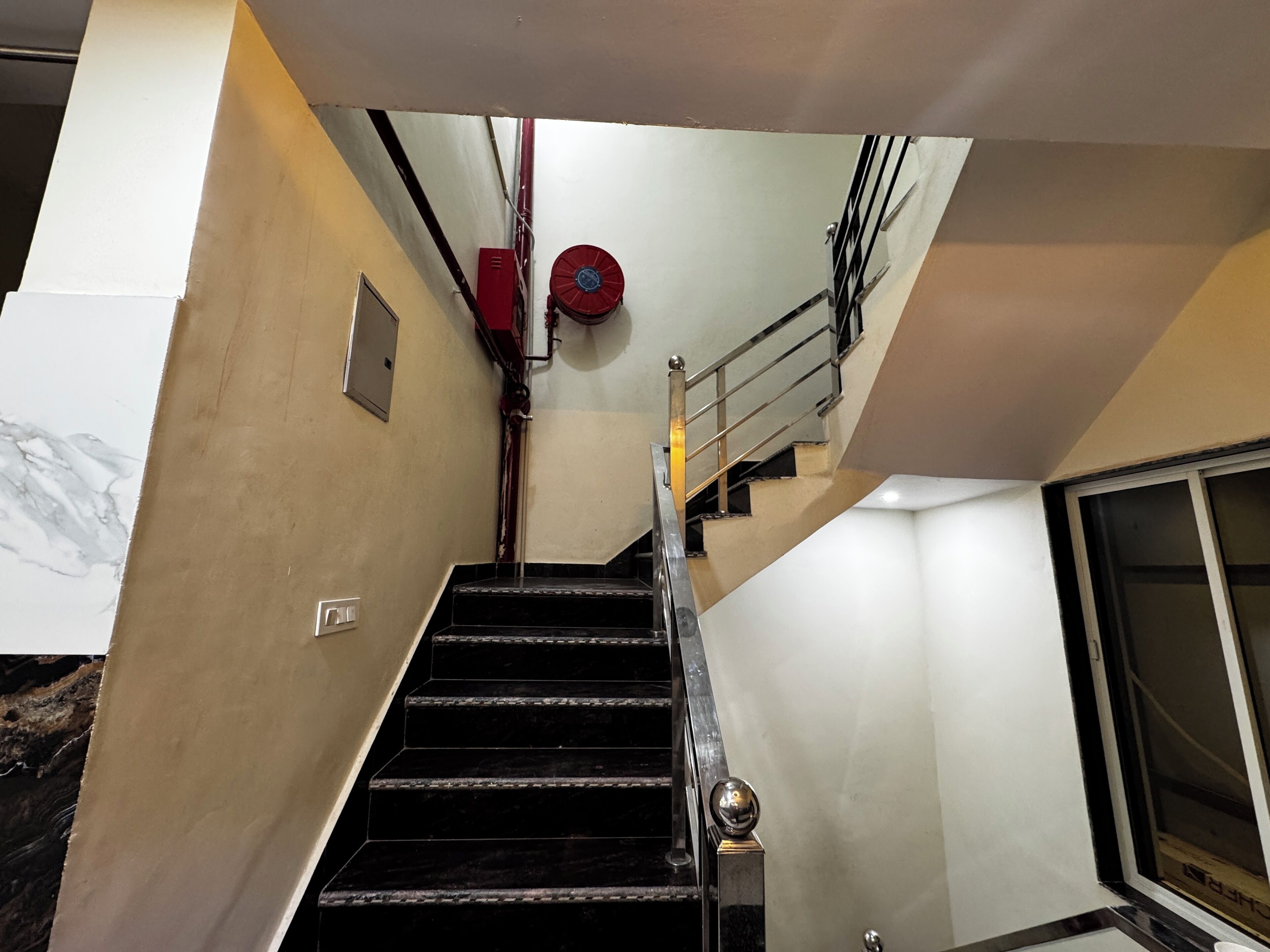 A staircase with black steps, a metal handrail, and a red fire extinguisher on the wall.
