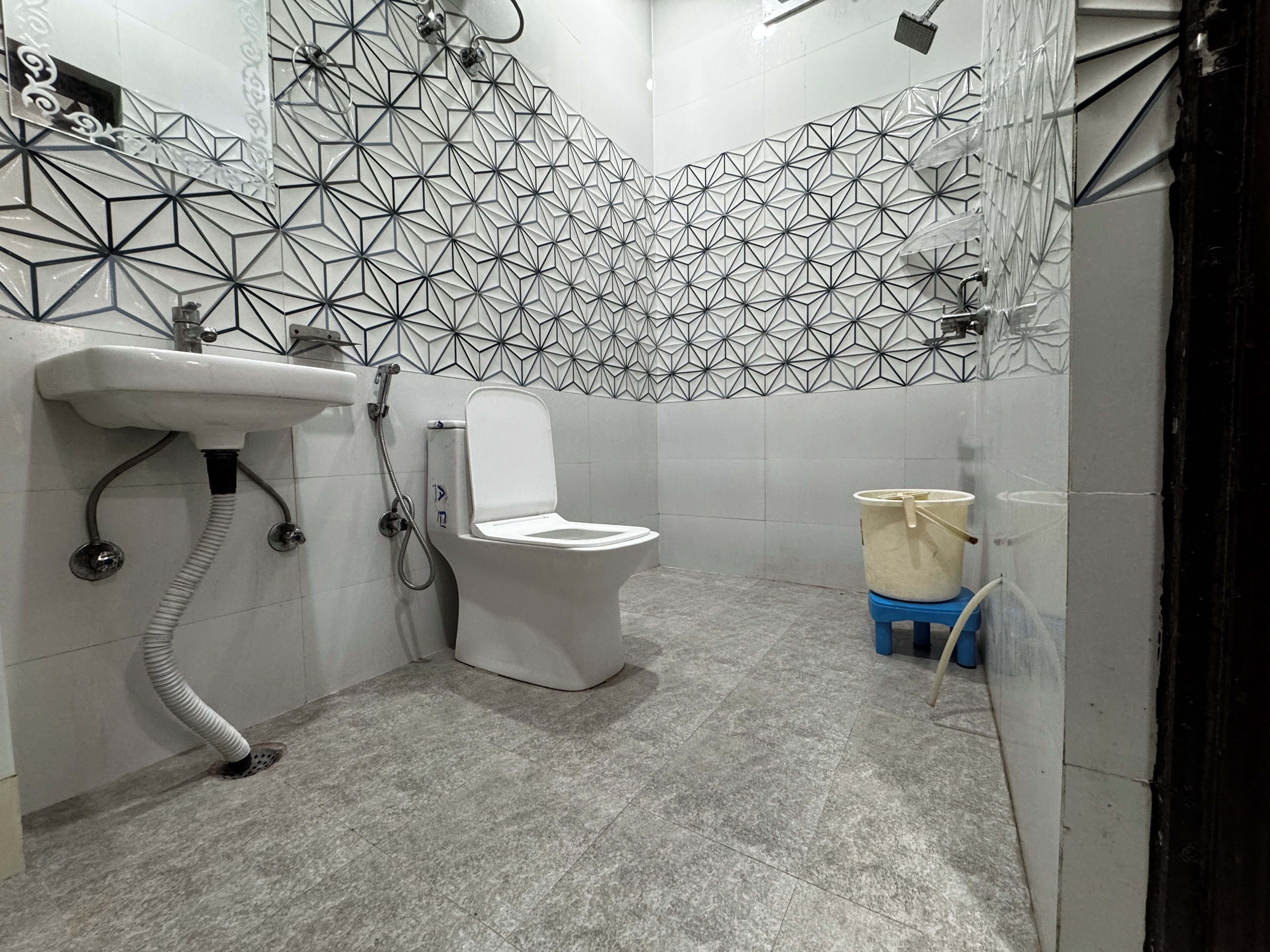 A bathroom with a toilet, a sink, and a shower. The walls have a geometric tile pattern.