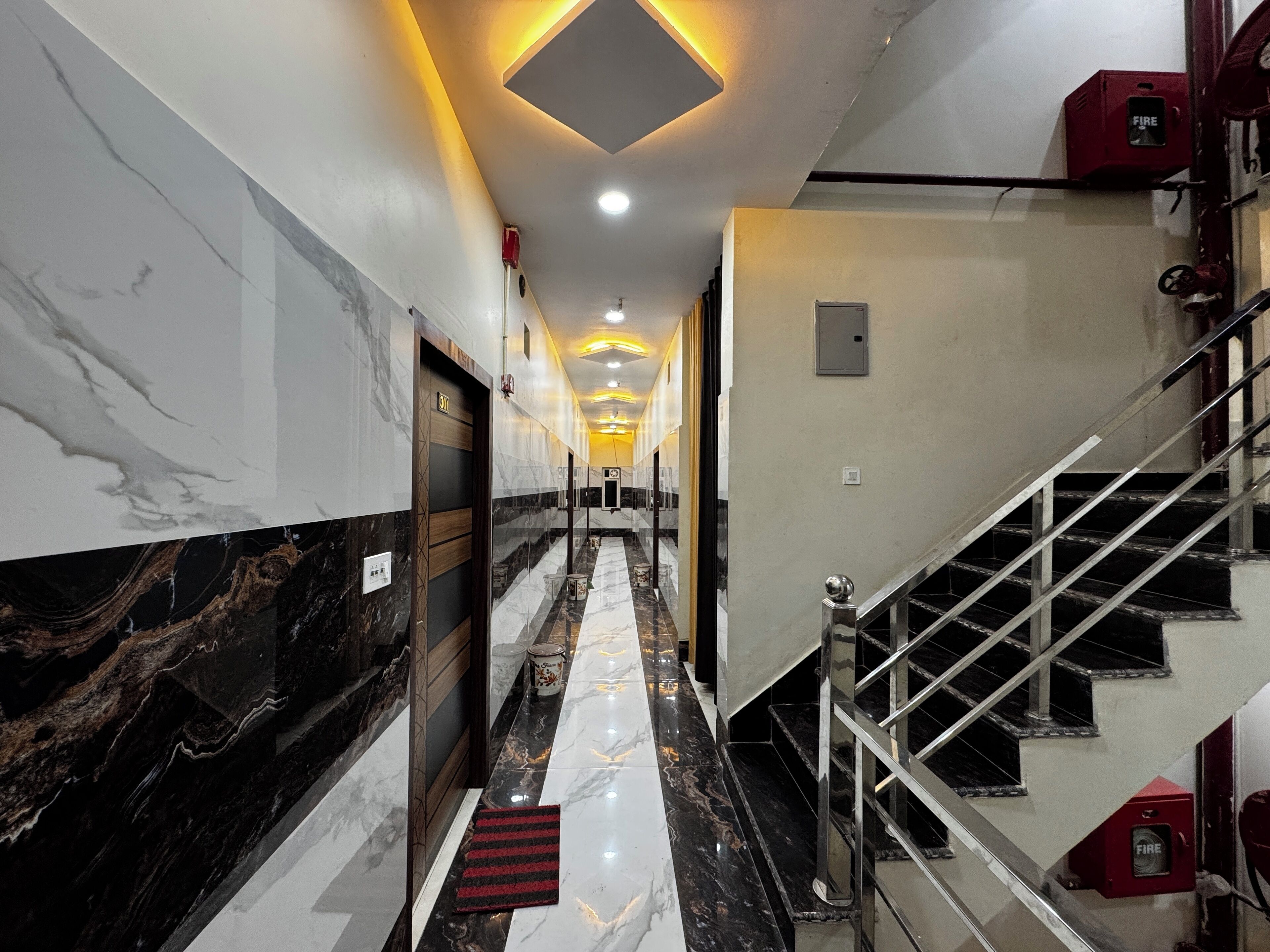 A hotel corridor with marble walls, a staircase, and a fire alarm.
