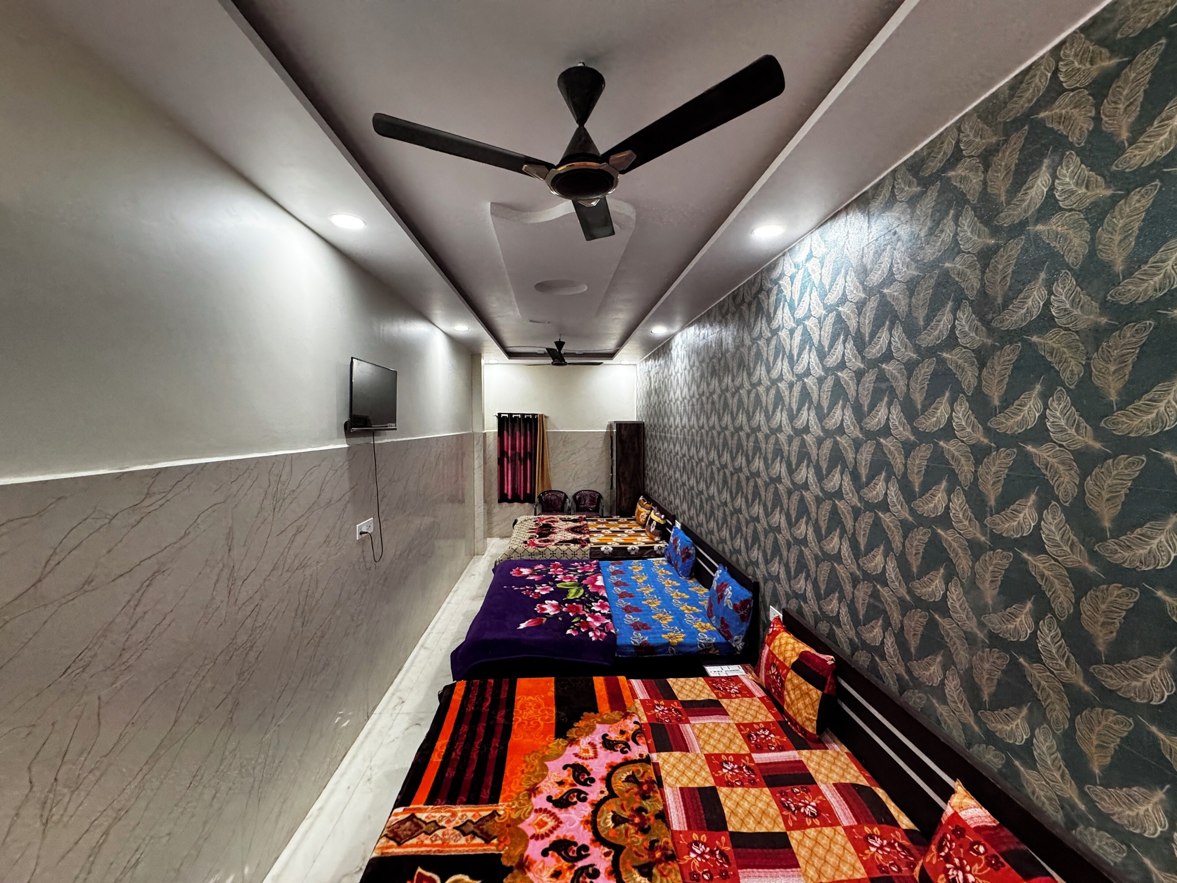 A narrow hotel corridor with a ceiling fan, a television mounted on the wall, and patterned wallpaper.