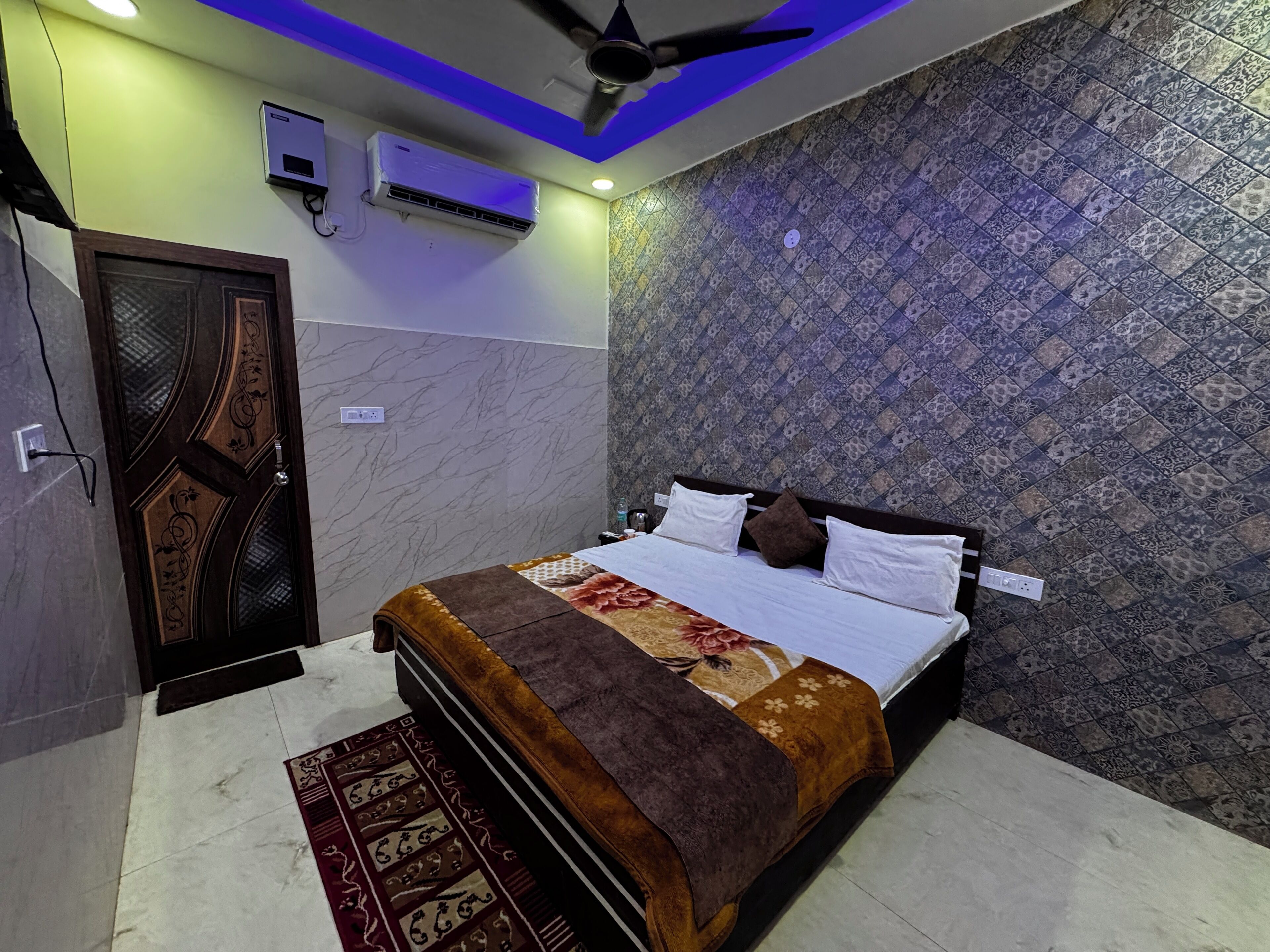 A bedroom with a bed, a ceiling fan, an air conditioner, patterned wallpaper, and a decorative rug.