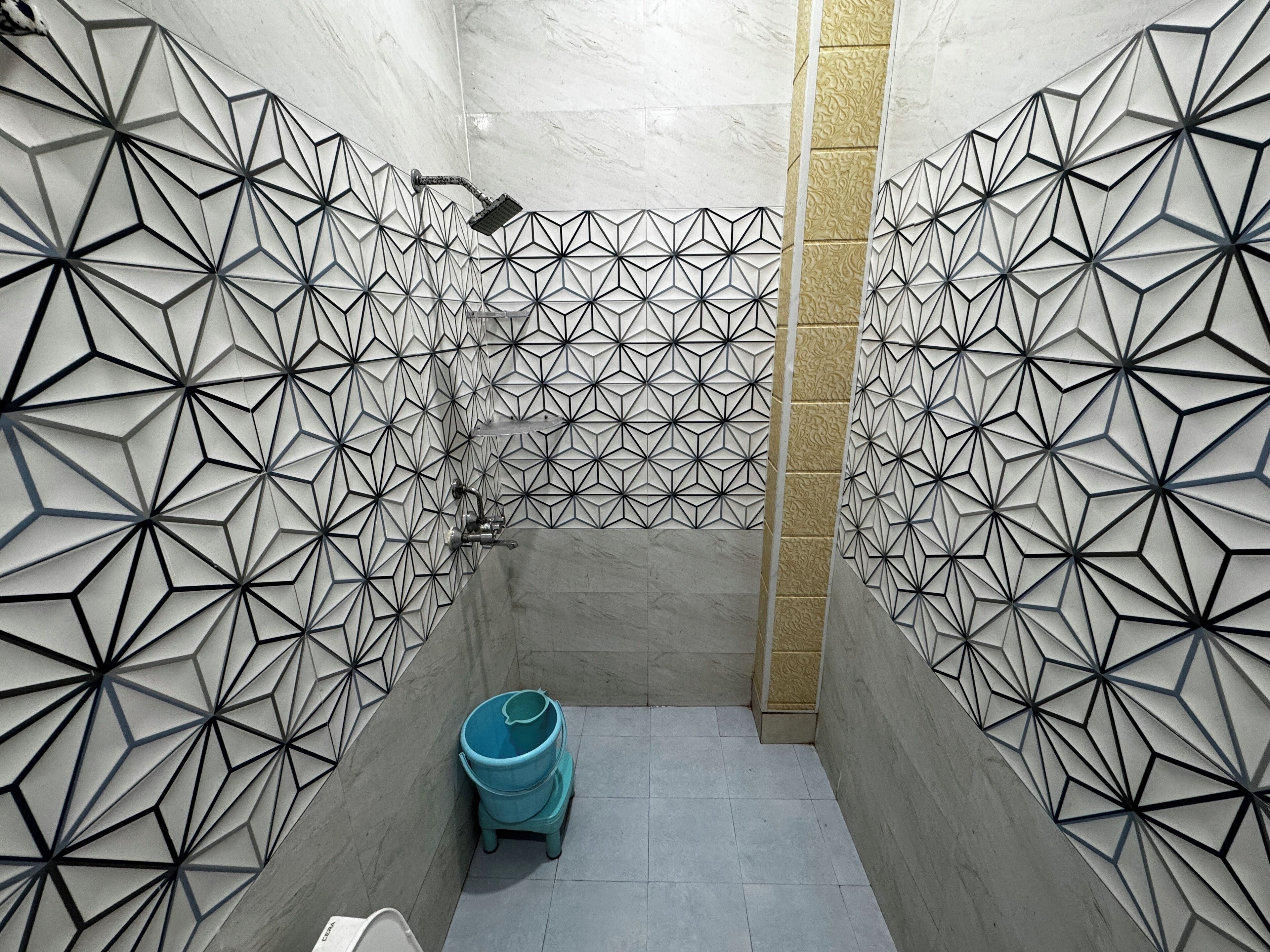 Een badkamer met geometrische wanddecoratie, een douche en een blauwe prullenbak.