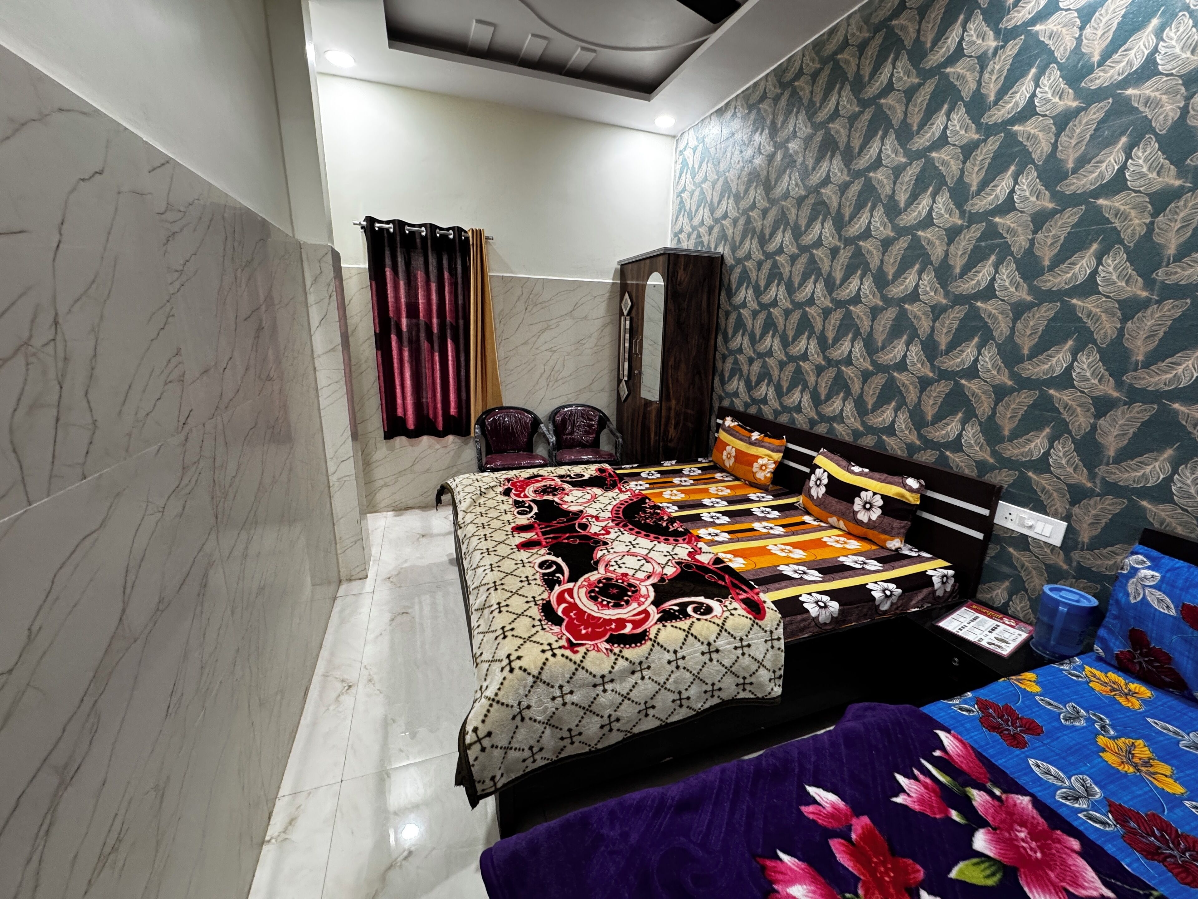 A bedroom with a bed, two chairs, a wardrobe, and patterned wallpaper.