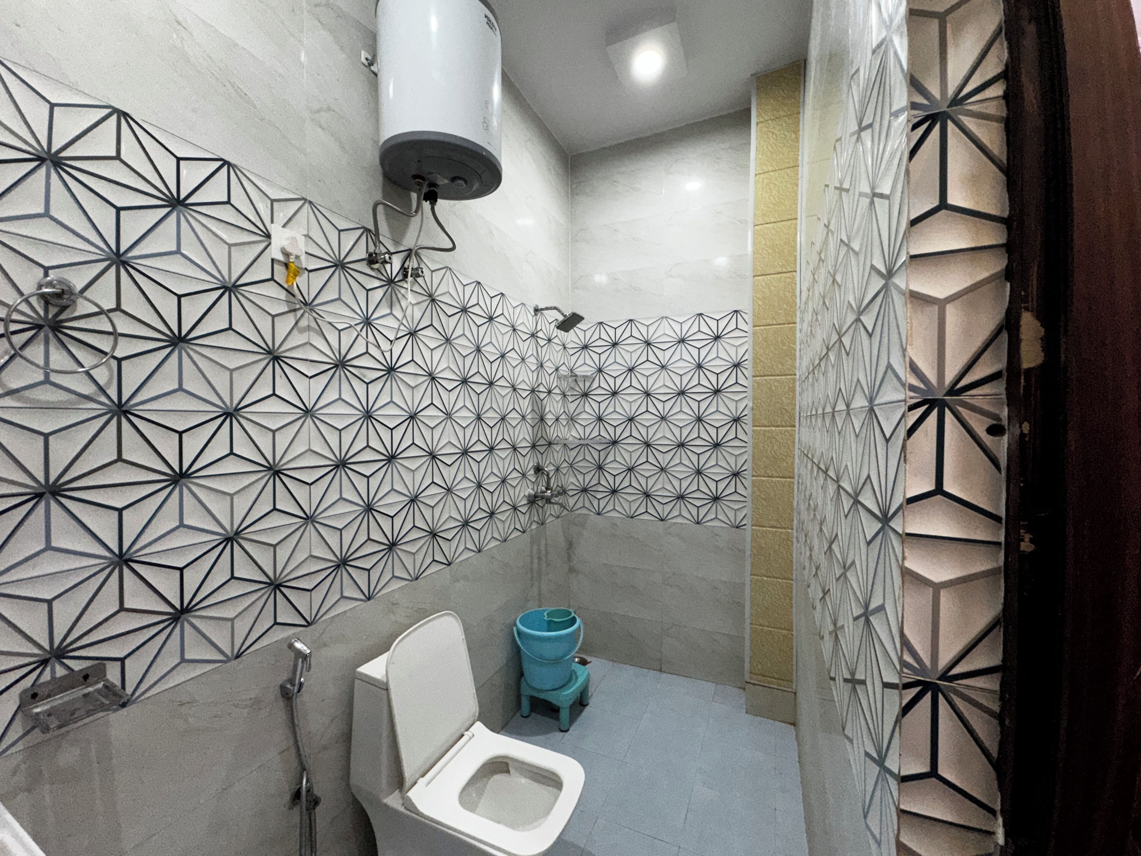 Un baño moderno con baldosas de diseño geométrico, un inodoro, una ducha y un dispensador de papel higiénico.