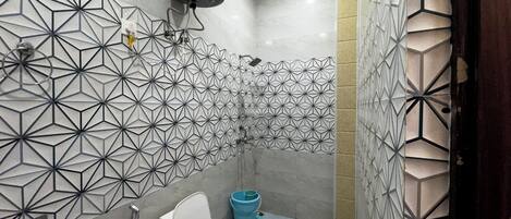 Un baño moderno con baldosas de diseño geométrico, un inodoro, una ducha y un dispensador de papel higiénico.