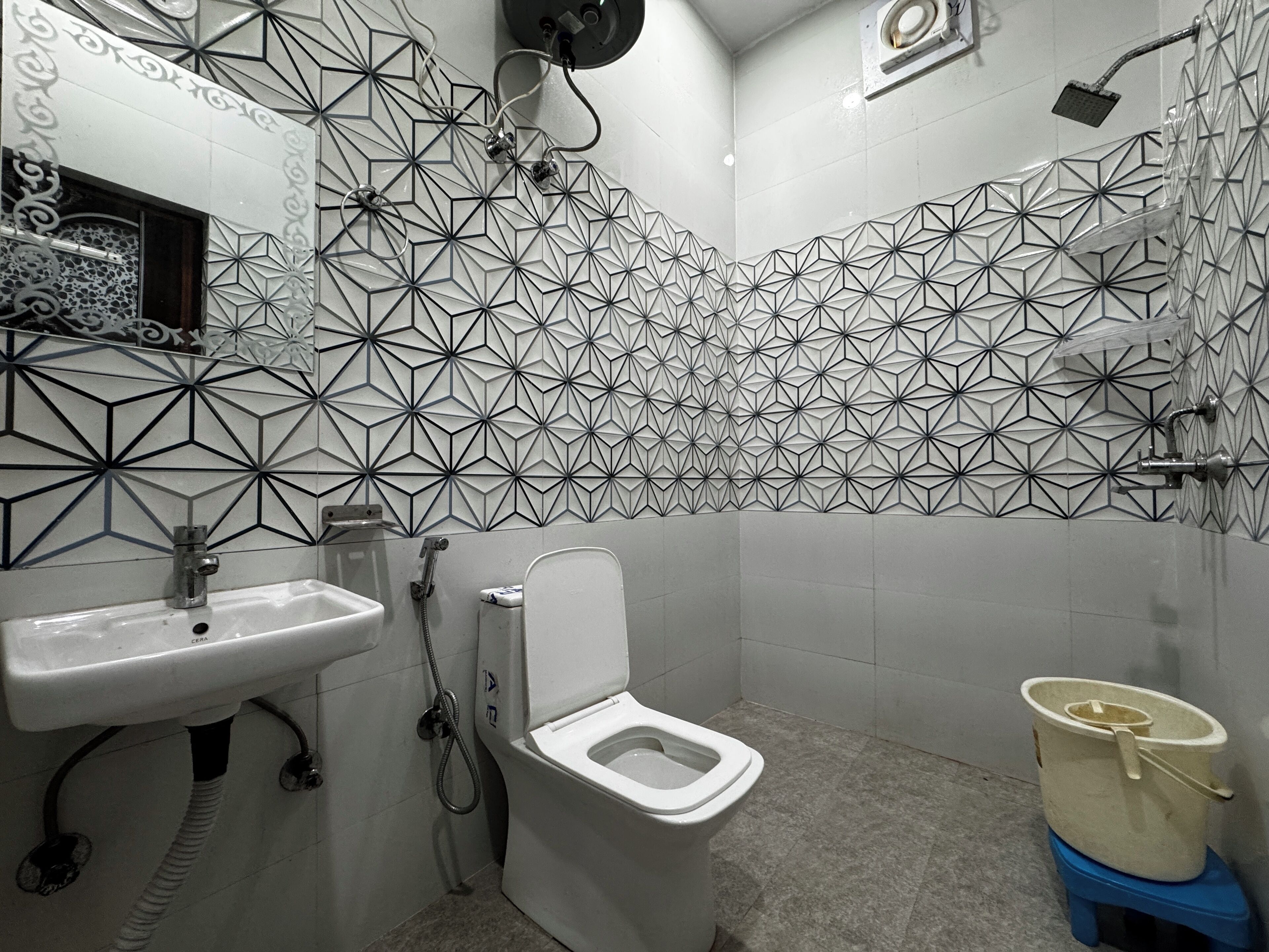 Un baño con pared de diseño geométrico, un lavabo blanco, un inodoro y una ducha.