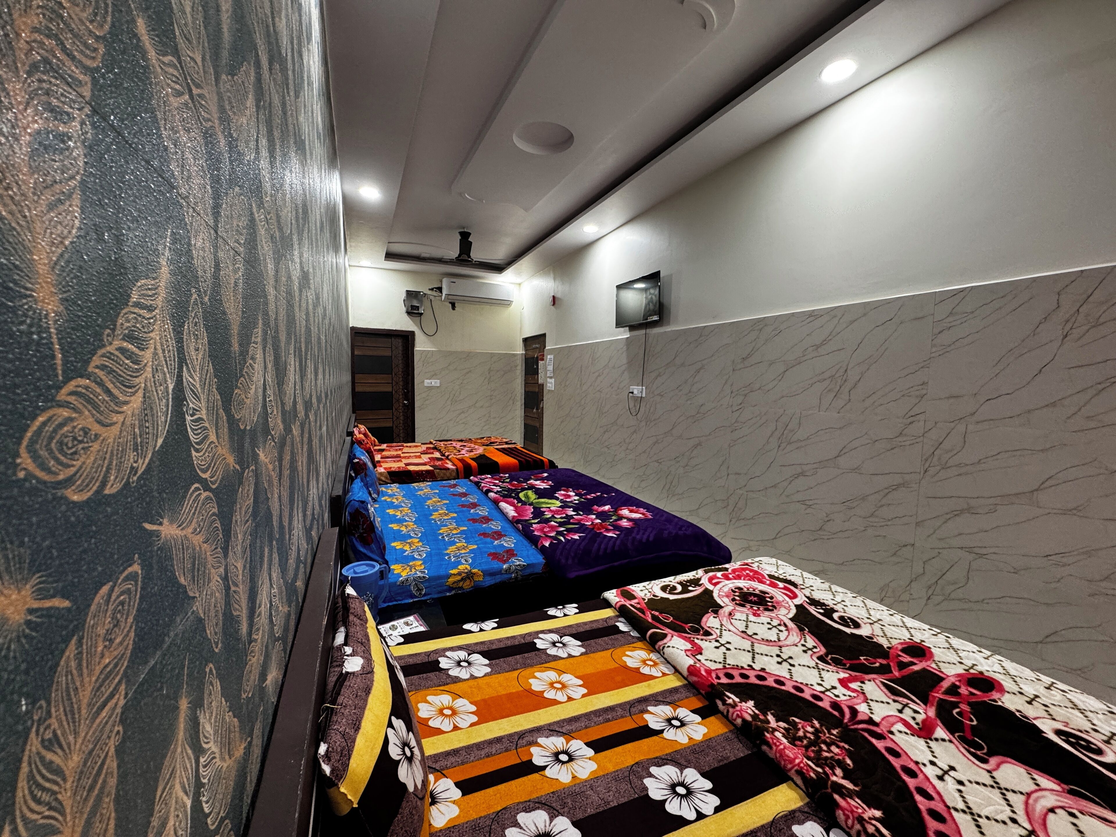 A hotel room with a long corridor, multiple beds with colorful bedding, a marble wall, and a ceiling with recessed lighting.