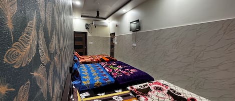 A hotel room with a long corridor, multiple beds with colorful bedding, a marble wall, and a ceiling with recessed lighting.