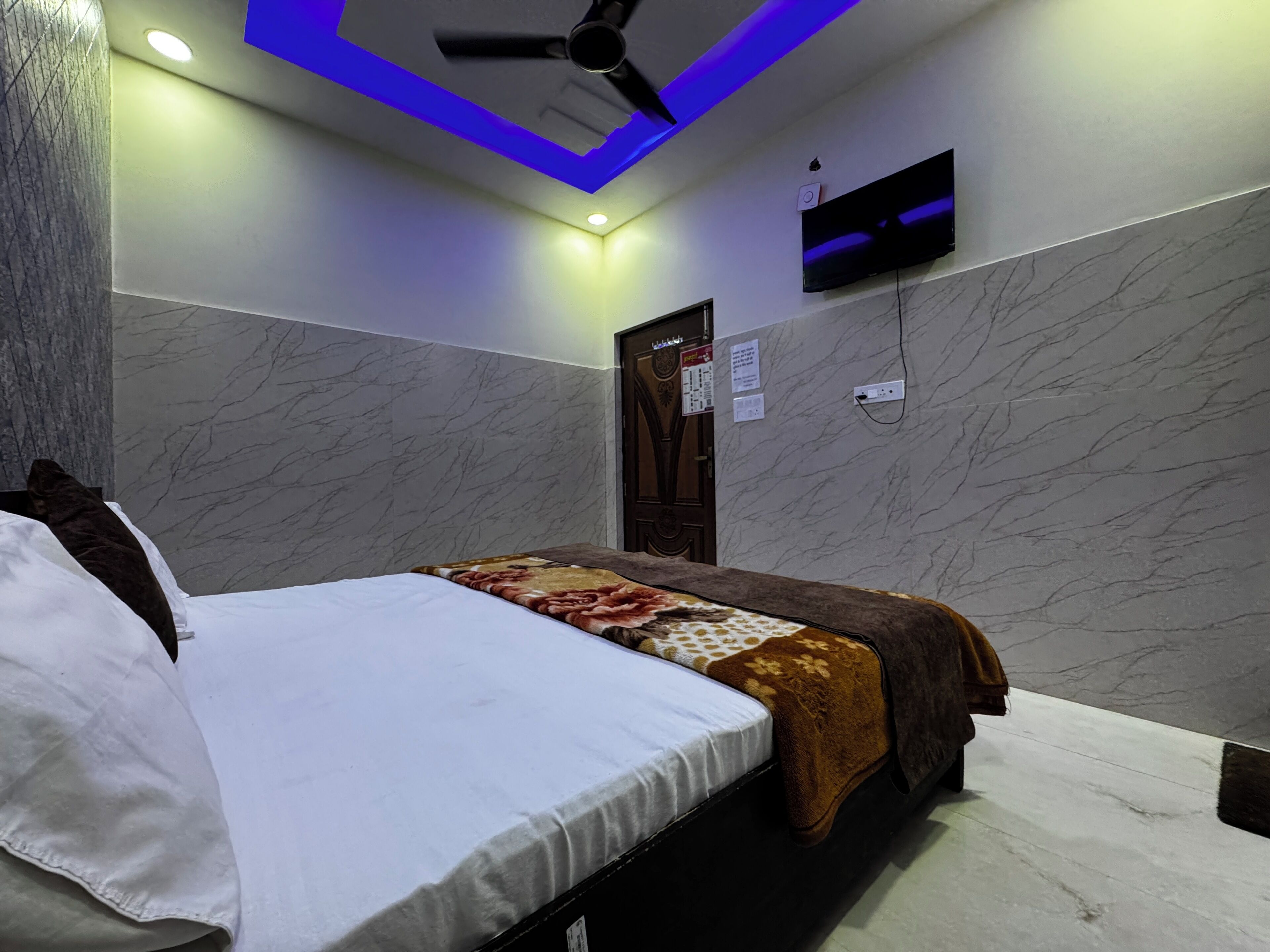 A bedroom with a bed, a ceiling fan, a TV mounted on the wall, and a door with a sign.