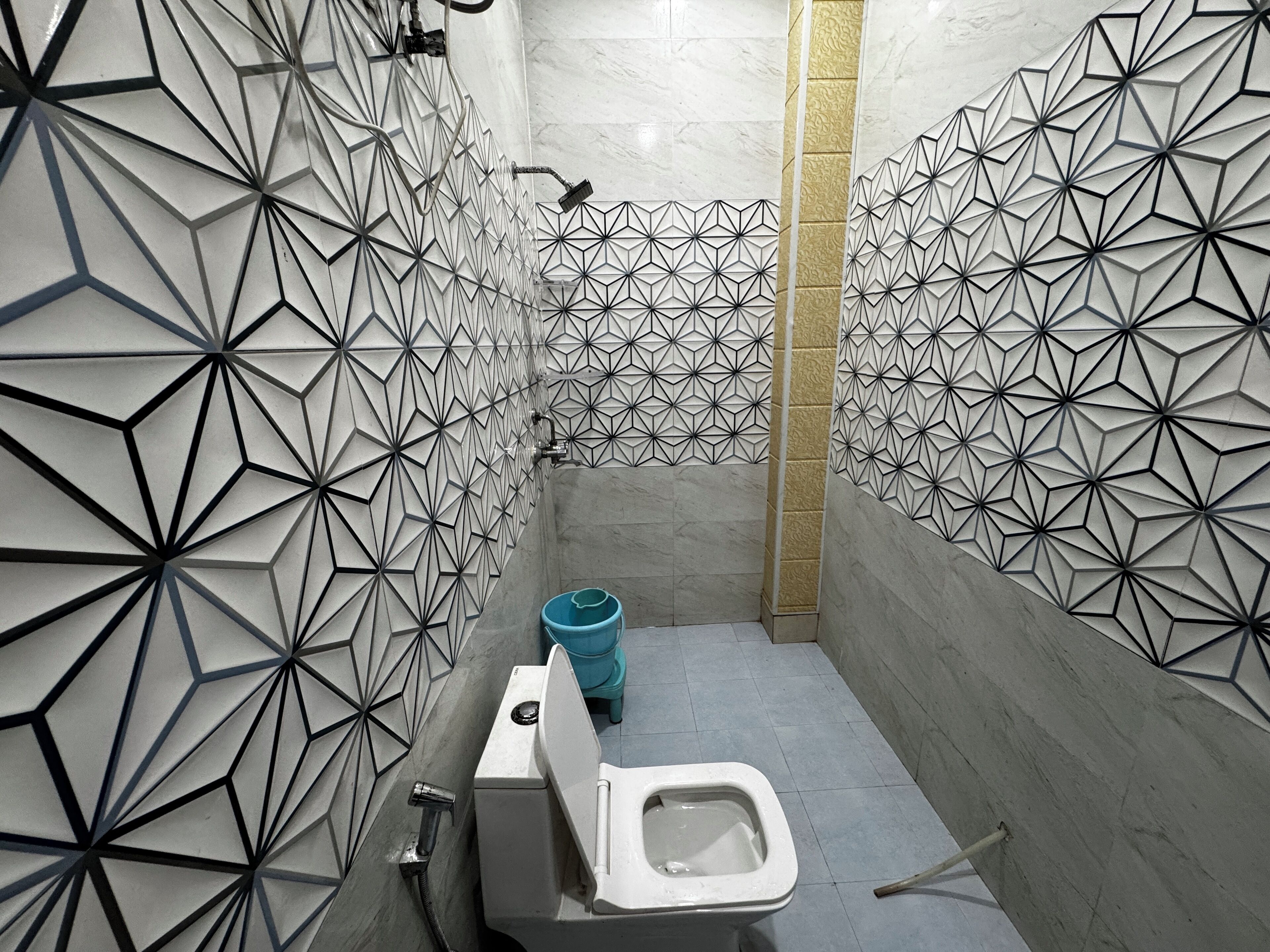 Un baño moderno con paredes de diseño geométrico, un inodoro y un cubo de basura azul.