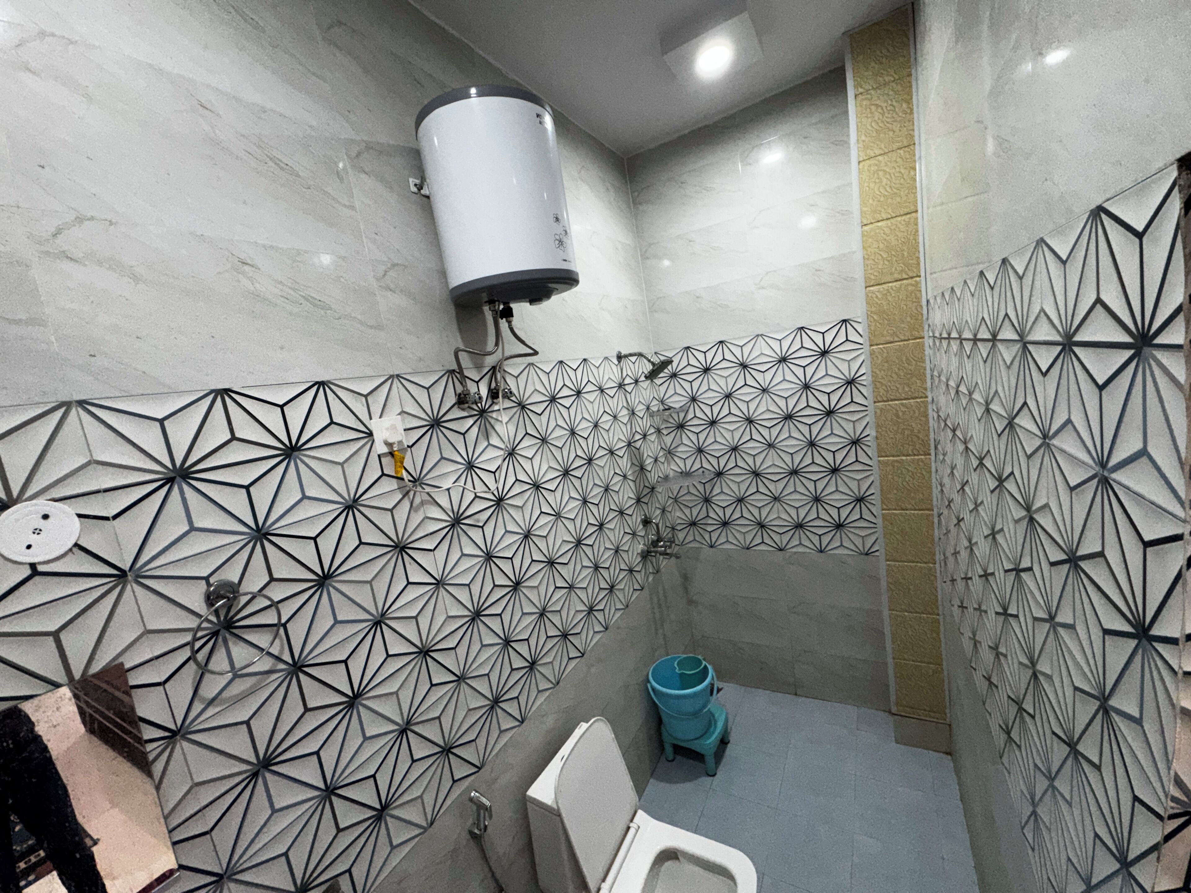 A modern bathroom with geometric patterned tiles, a white toilet, and a blue trash bin.