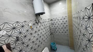 A modern bathroom with geometric patterned tiles, a white toilet, and a blue trash bin.