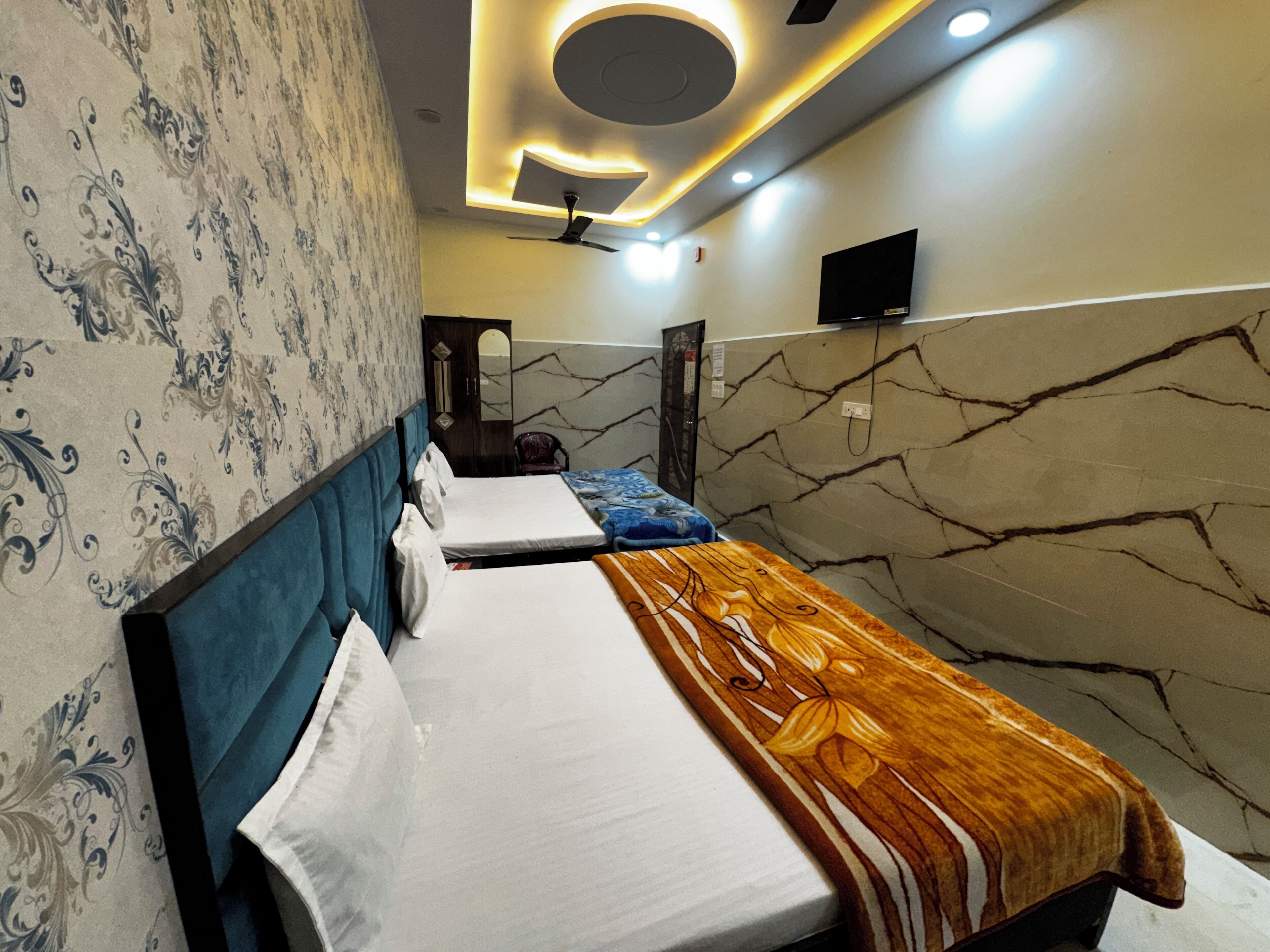 Une chambre d’hôtel avec deux lits, un ventilateur de plafond, une télévision et des murs décorés d’un motif marbré.