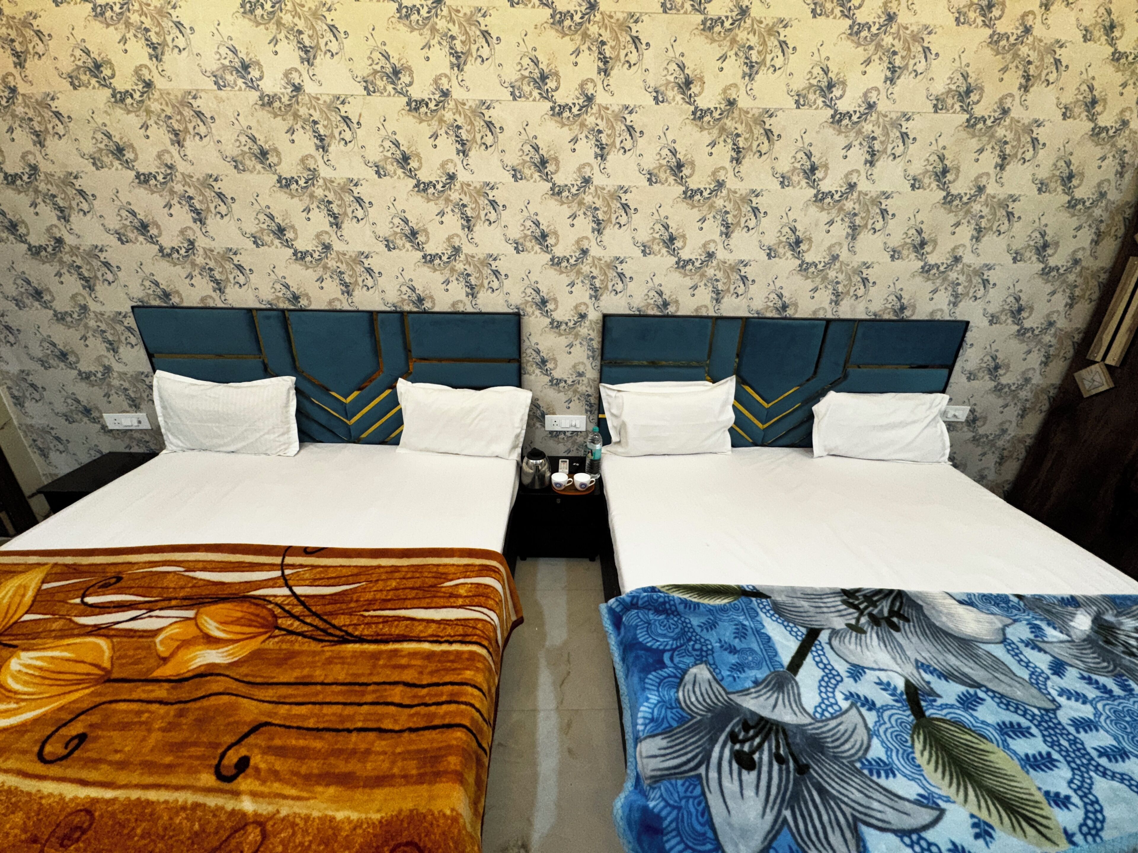 Two twin beds with headboards, white bedding, and a floral wallpaper pattern.