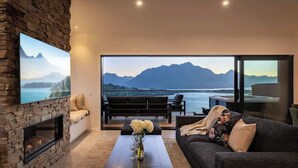 A living room with a stone fireplace, a sofa, a coffee table with flowers, and a large window with a mountain view.