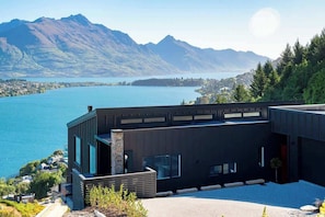 A modern building with large windows overlooking a lake and mountains. - Summit Escape, Hot Tub, Fireplace, BBQ, AC & Views (Queenstown)