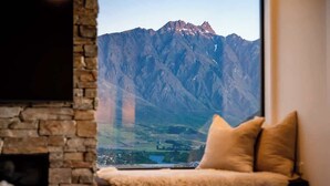 A room with a stone fireplace, a view of a mountain, and a fur-covered chair.