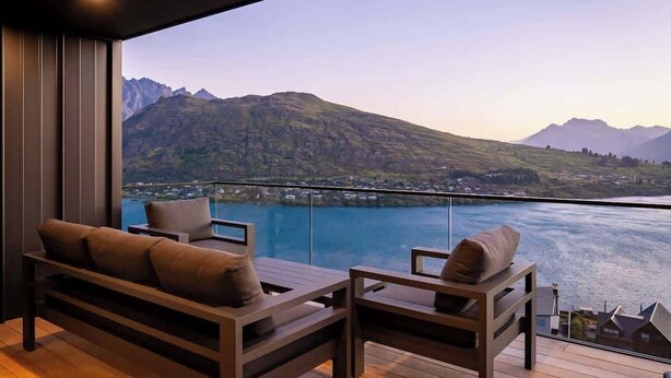 A balcony with a view of a lake and mountains, furnished with a sofa and chairs. - Summit Escape, Hot Tub, Fireplace, BBQ, AC & Views (Queenstown)