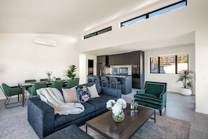 A modern living room with a sofa, coffee table, and dining area. - Summit Escape, Hot Tub, Fireplace, BBQ, AC & Views (Queenstown)