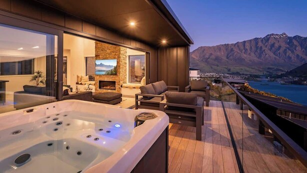A modern outdoor living area with a hot tub, seating, and a scenic mountain view.