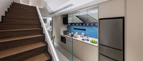 Una cocina moderna con un refrigerador de acero inoxidable, una escalera de vidrio y un salpicadero azul.