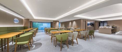 A modern dining area with multiple tables and chairs, a kitchen area, and a large window providing a view of the outdoors.