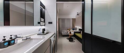 Een moderne hotelbadkamer met een grote spiegel, een wastafel met zeepdispensers, een toilet en een douchegedeelte.