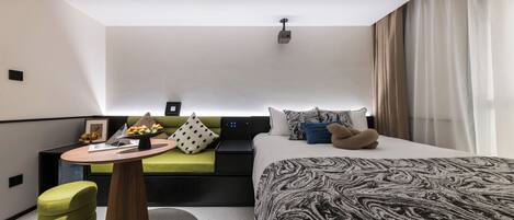 A modern hotel room with a bed, a sofa, a small table with a vase of flowers, and a projector on the ceiling.
