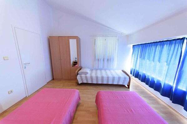 Une chambre avec deux lits simples, une armoire en bois, un miroir et une fenêtre avec des rideaux bleus.