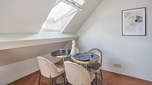A dining area with a table and chairs, a skylight, and a framed artwork on the wall. - New Apartment Center of Paris/le Marais (Paris)