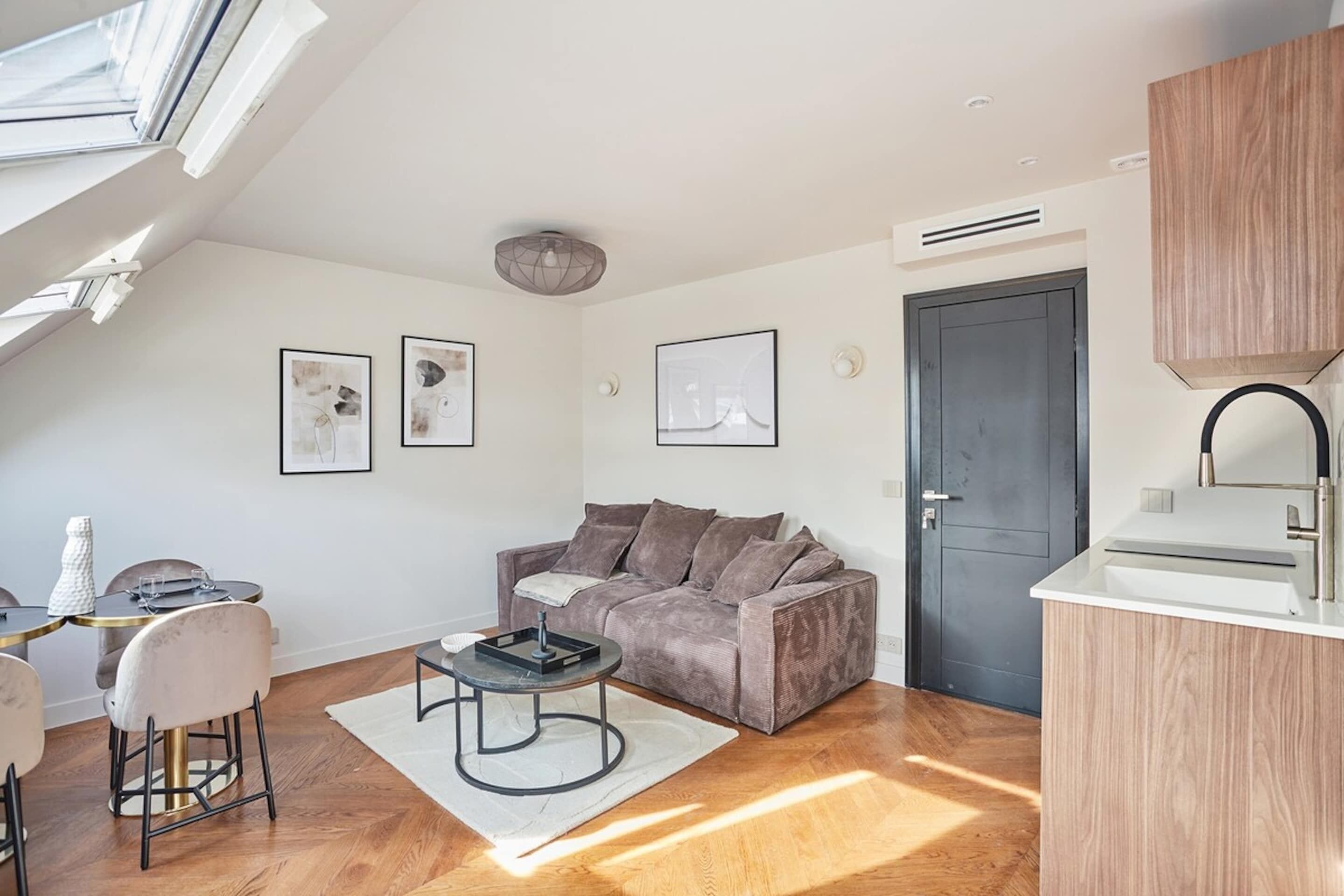 A modern living room with a sofa, coffee table, and dining area. There is a door and a window with a view.