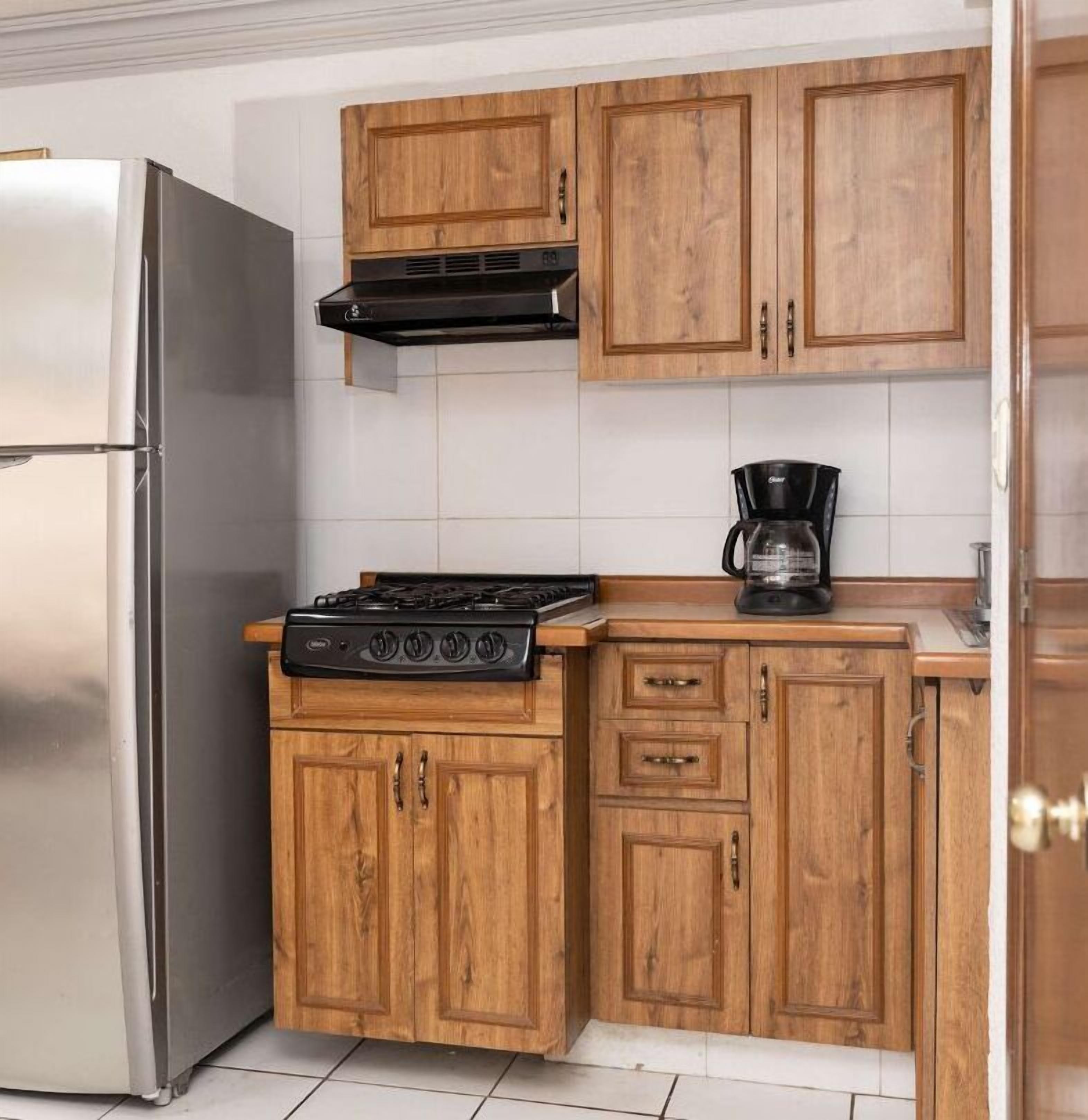 A kitchen with wooden cabinets, a stainless steel refrigerator, a gas stove, and a coffee maker.