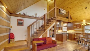 Un interior espacioso de madera con una escalera que conduce a un altillo, un comedor y una cocina.