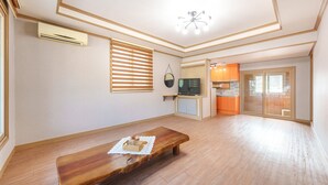 A spacious living room with a wooden bench, a TV, and a kitchen area visible through an open door. - Gyeongju Beach Castle Pension (Gyeongju)