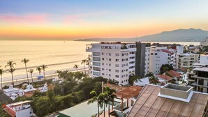 Ein Hotel an der Küste mit mehreren Etagen, einem Pool und Blick auf den Strand und das Meer bei Sonnenuntergang.