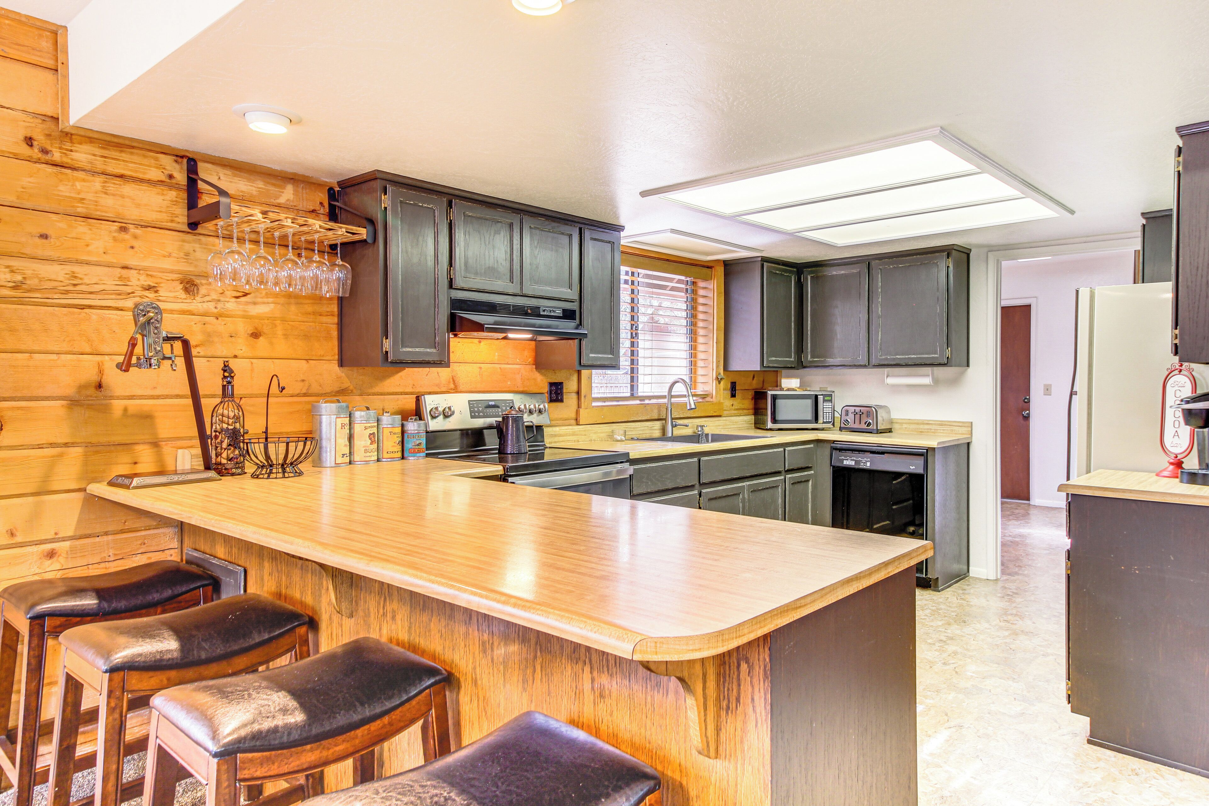 A kitchen with wooden cabinets, a central island with stools, a microwave, and a refrigerator.