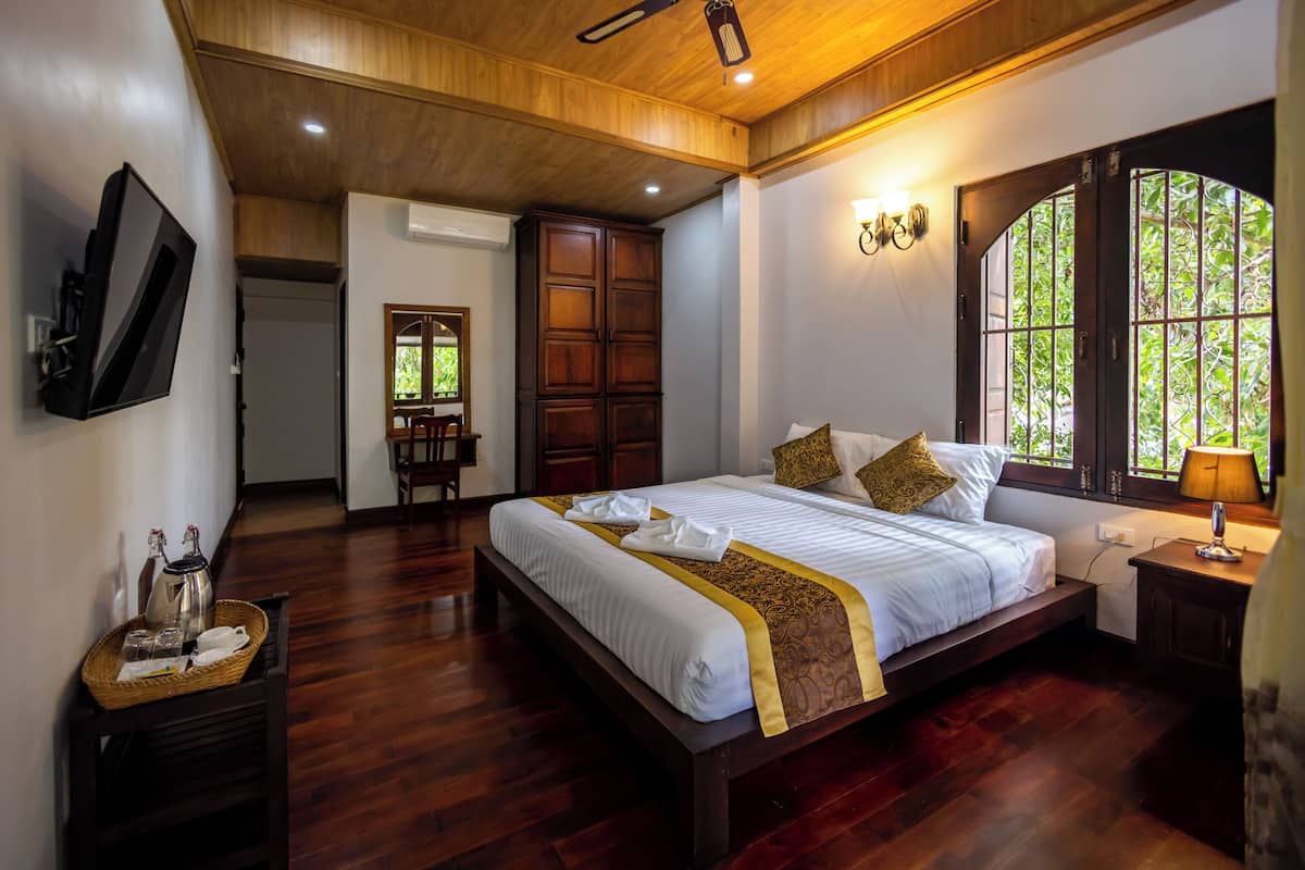 Une chambre spacieuse avec un grand lit, un plancher en bois, un téléviseur fixé au mur et une fenêtre donnant sur un paysage verdoyant.