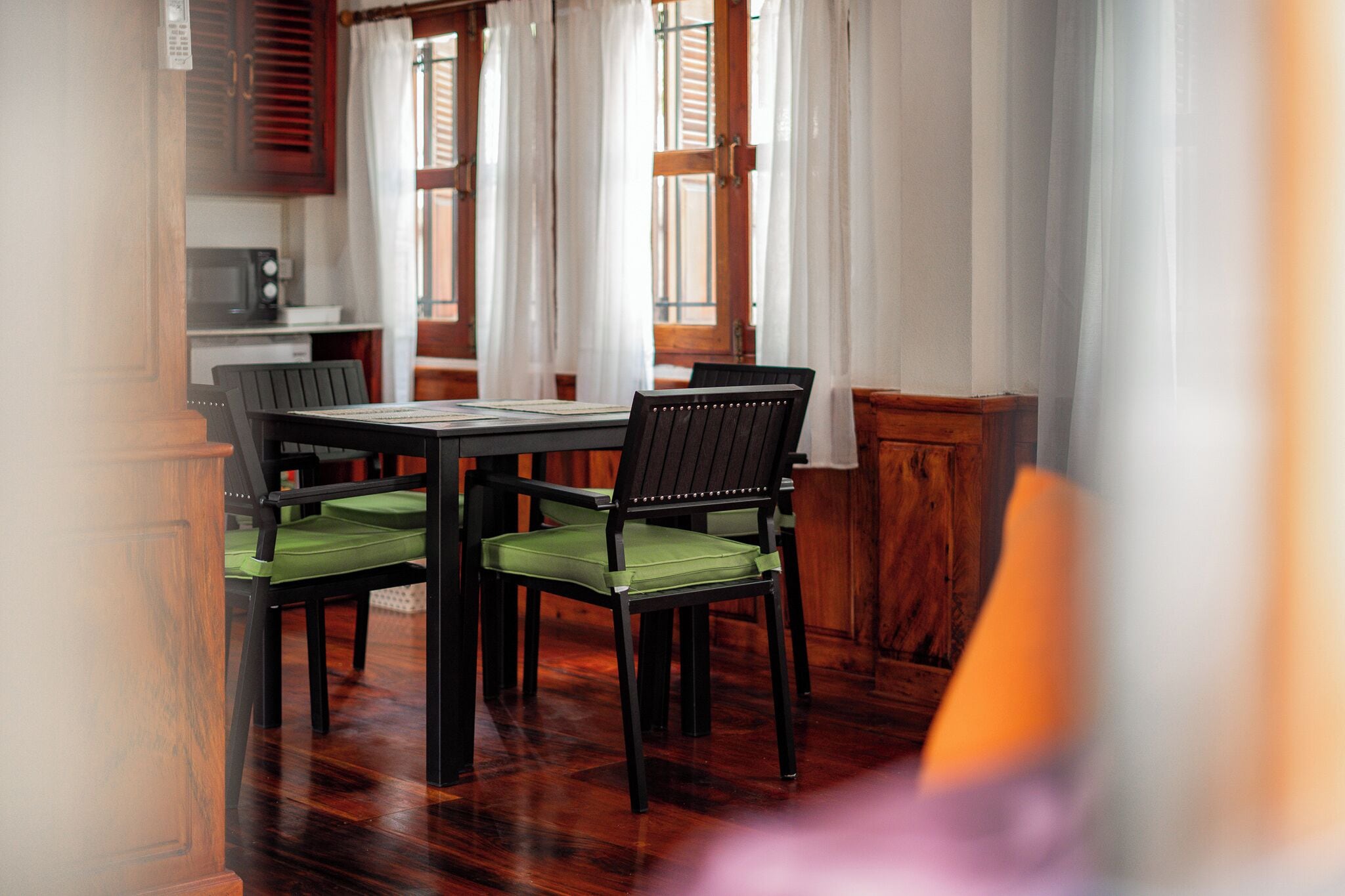 Zona pranzo con tavolo e sedie in legno, un forno a microonde e vista attraverso una finestra con persiane di legno.