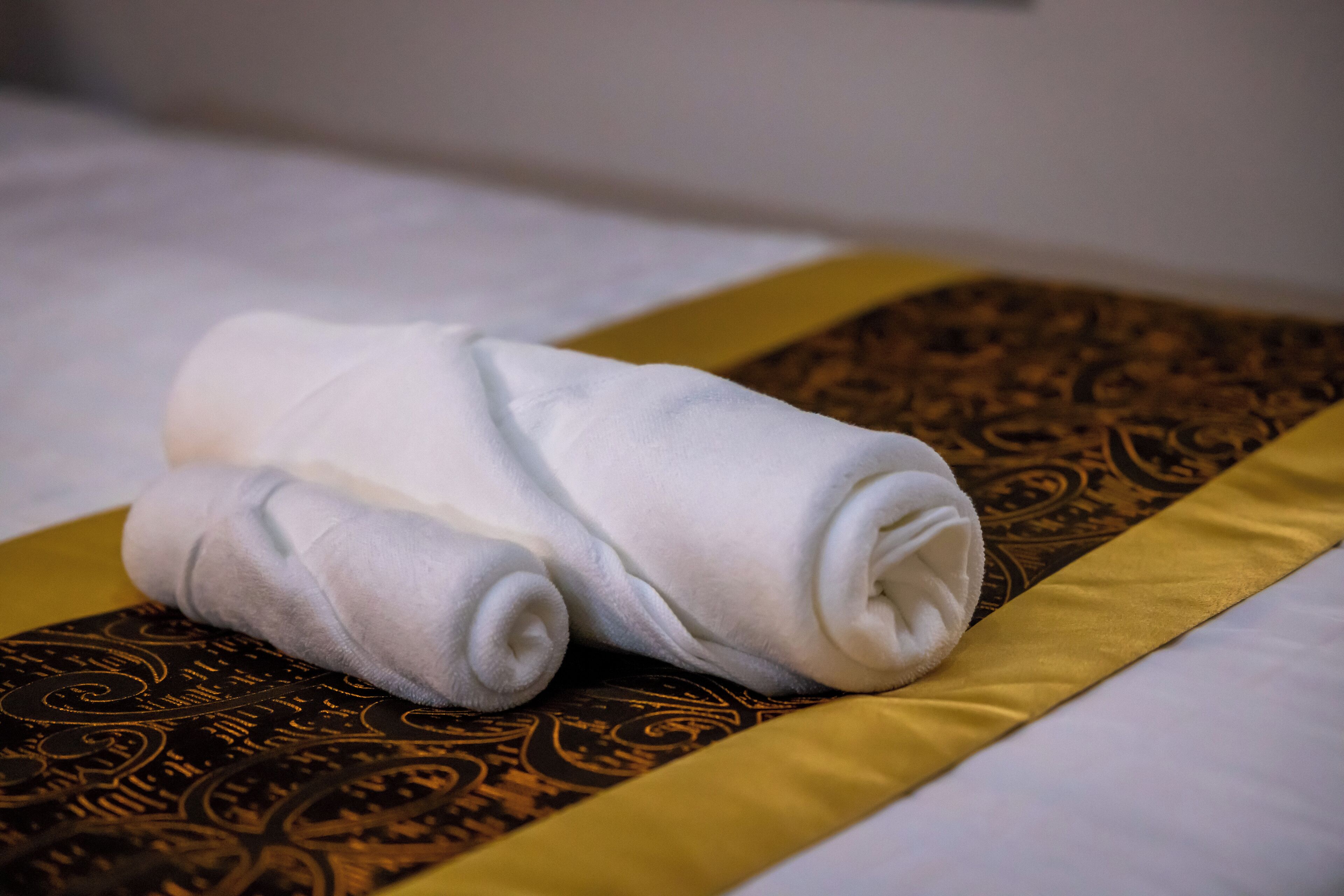 Ein ordentlich gefaltetes weißes Handtuch auf einem Bett mit einer braunen und goldenen Tagesdecke mit Muster.