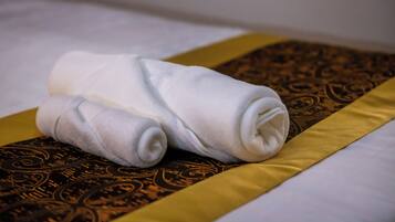 Une serviette blanche, soigneusement pliée, est posée sur un lit recouvert d’une couverture à motifs marron et doré.