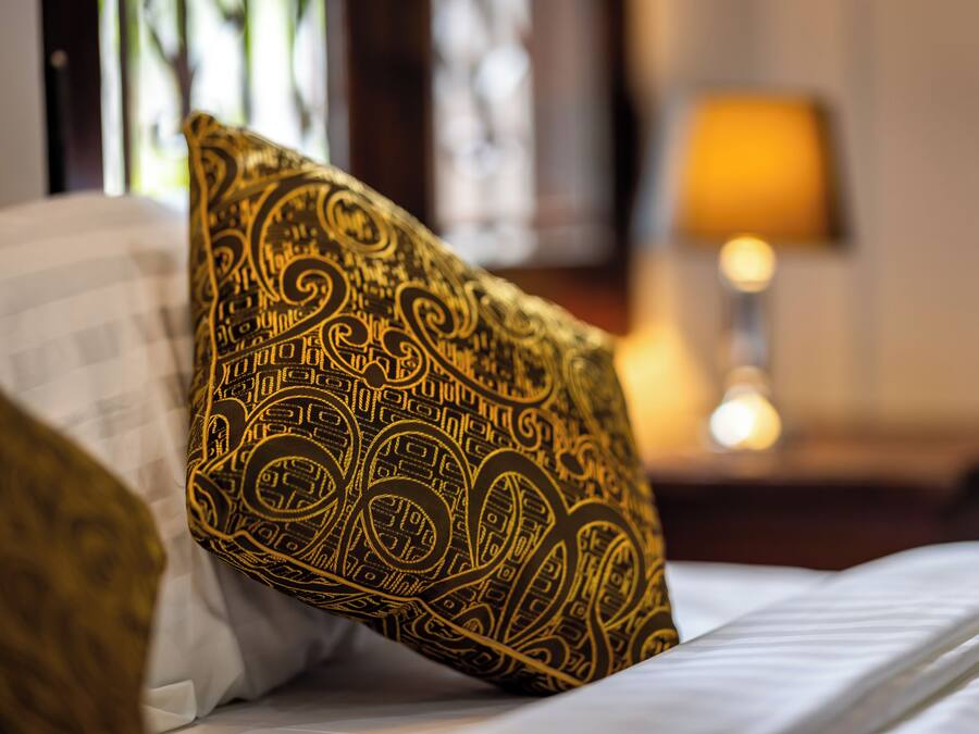 Una cama con un cojín estampado y una lámpara al fondo.