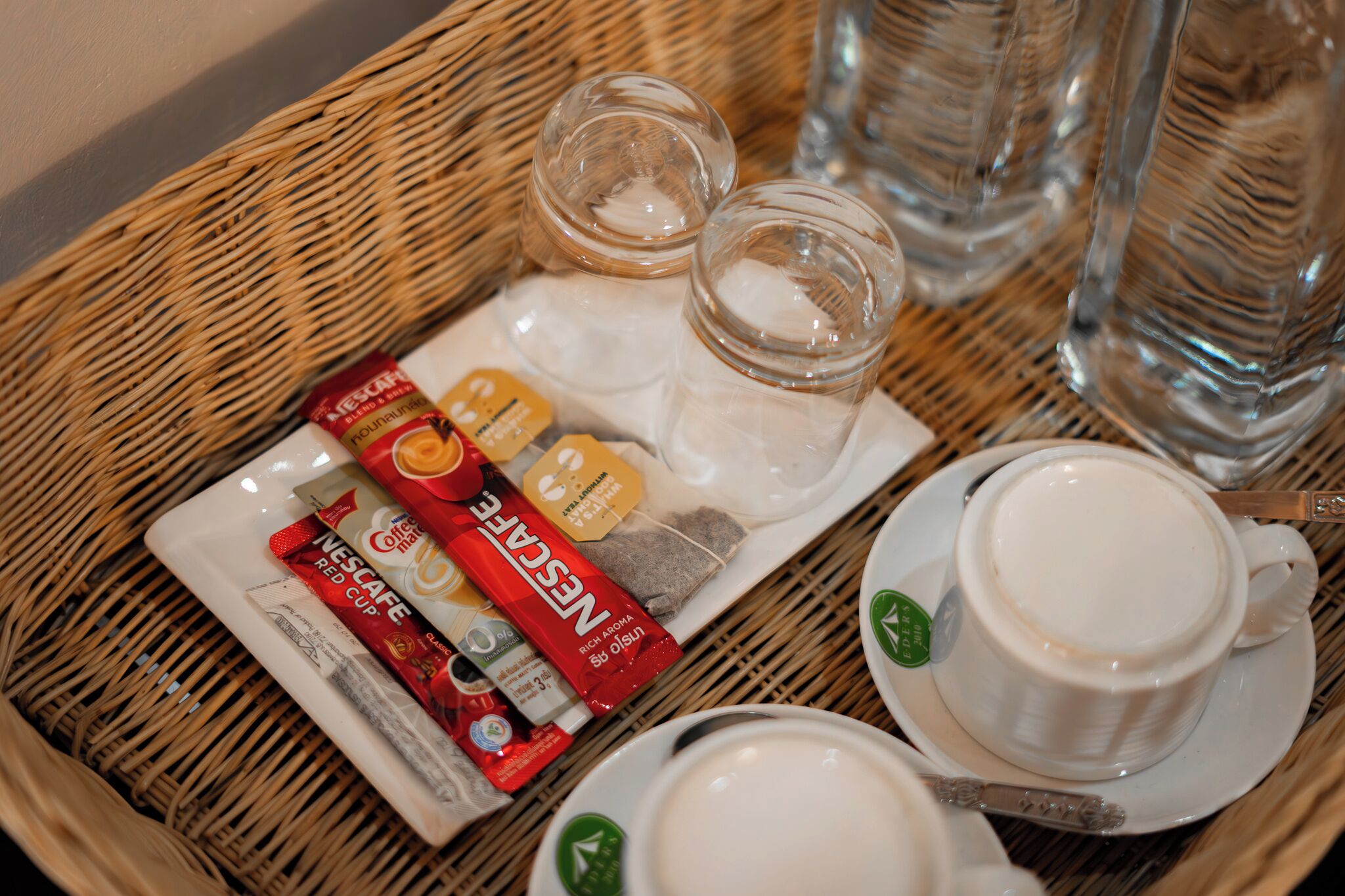 Una bandeja con un sobre de Nescafé Red Cup, un frasco pequeño de vidrio y una taza blanca sobre una mesa de mimbre.
