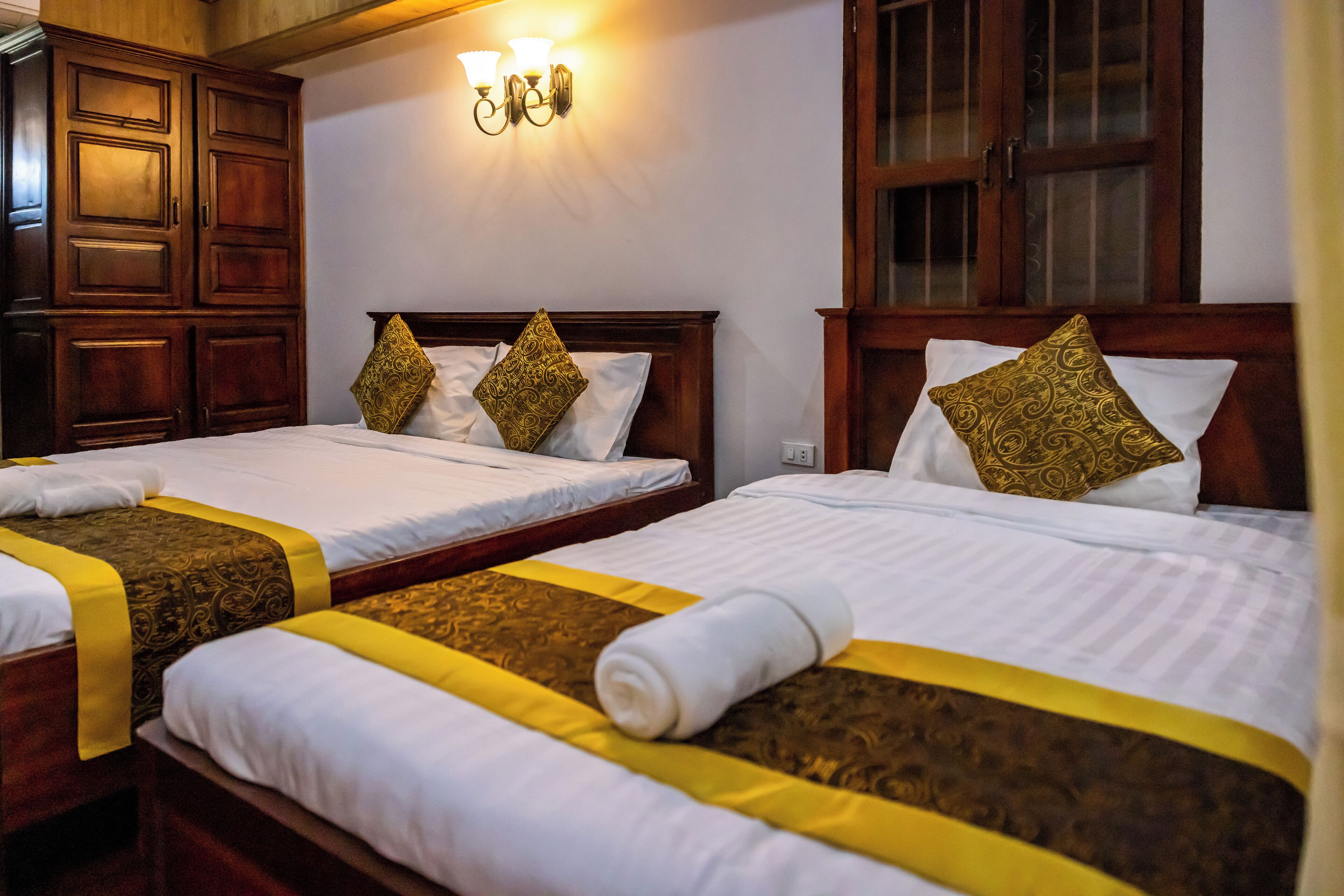 Ein Hotelzimmer mit zwei Betten, jeweils mit Kopfteil und dekorativen Kissen. Über den Betten befindet sich eine wandmontierte Leuchte.