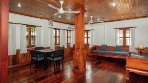 Une pièce spacieuse avec un plancher en bois, une table à manger avec des chaises, un canapé et deux ventilateurs de plafond.