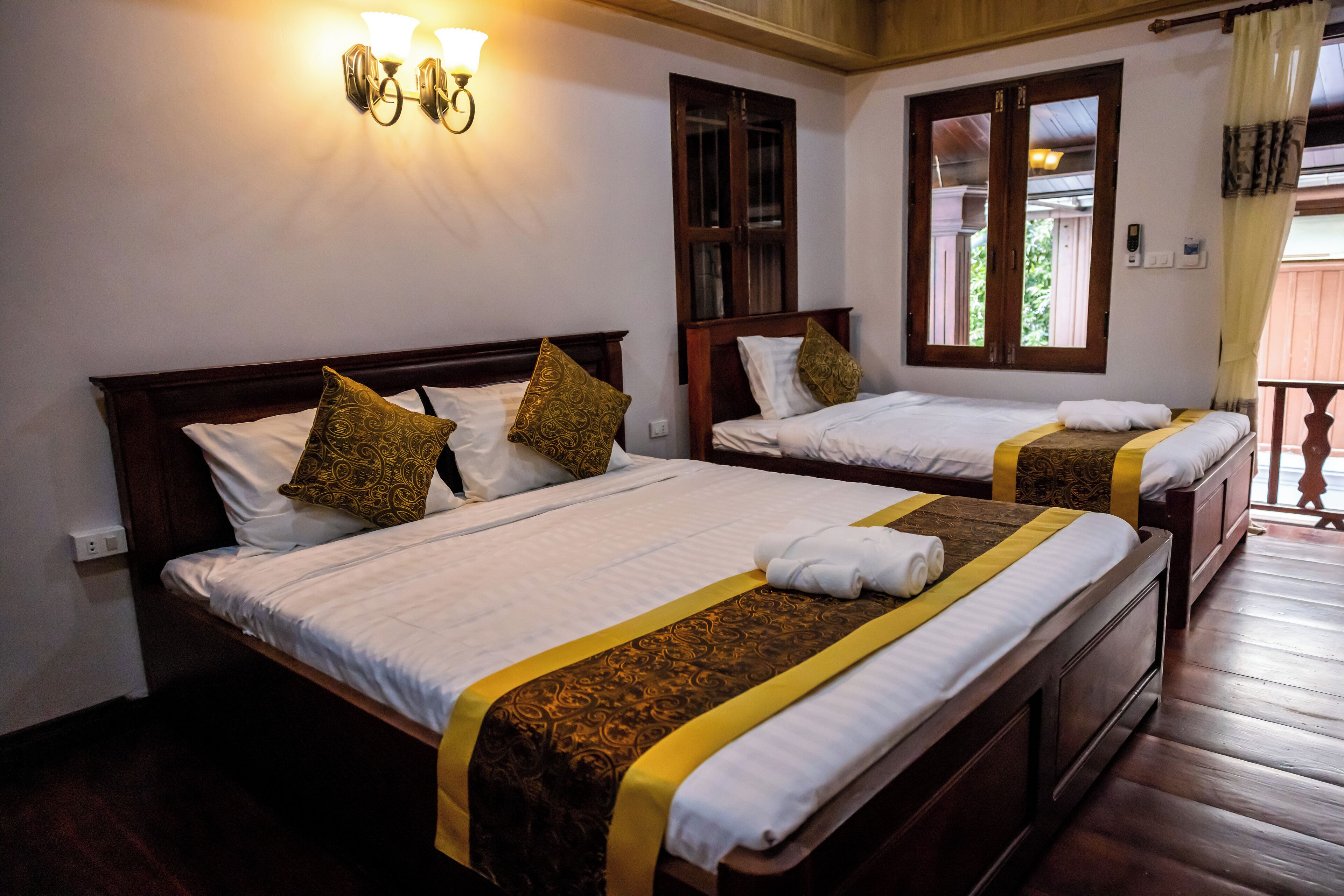 Habitación de hotel con dos camas, cada una con cabecero de madera, sábanas blancas y almohadas decorativas. Se ve un ventanal con vistas a zonas verdes.