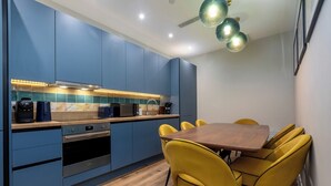 A modern kitchen with blue cabinets, a wooden countertop, and a dining table with yellow chairs. - Palm Tree House | Van Gogh (Greater London)